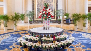 Um hall de entrada com um grande candelabro, uma mesa redonda com arranjos florais e uma grande pintura na parede.