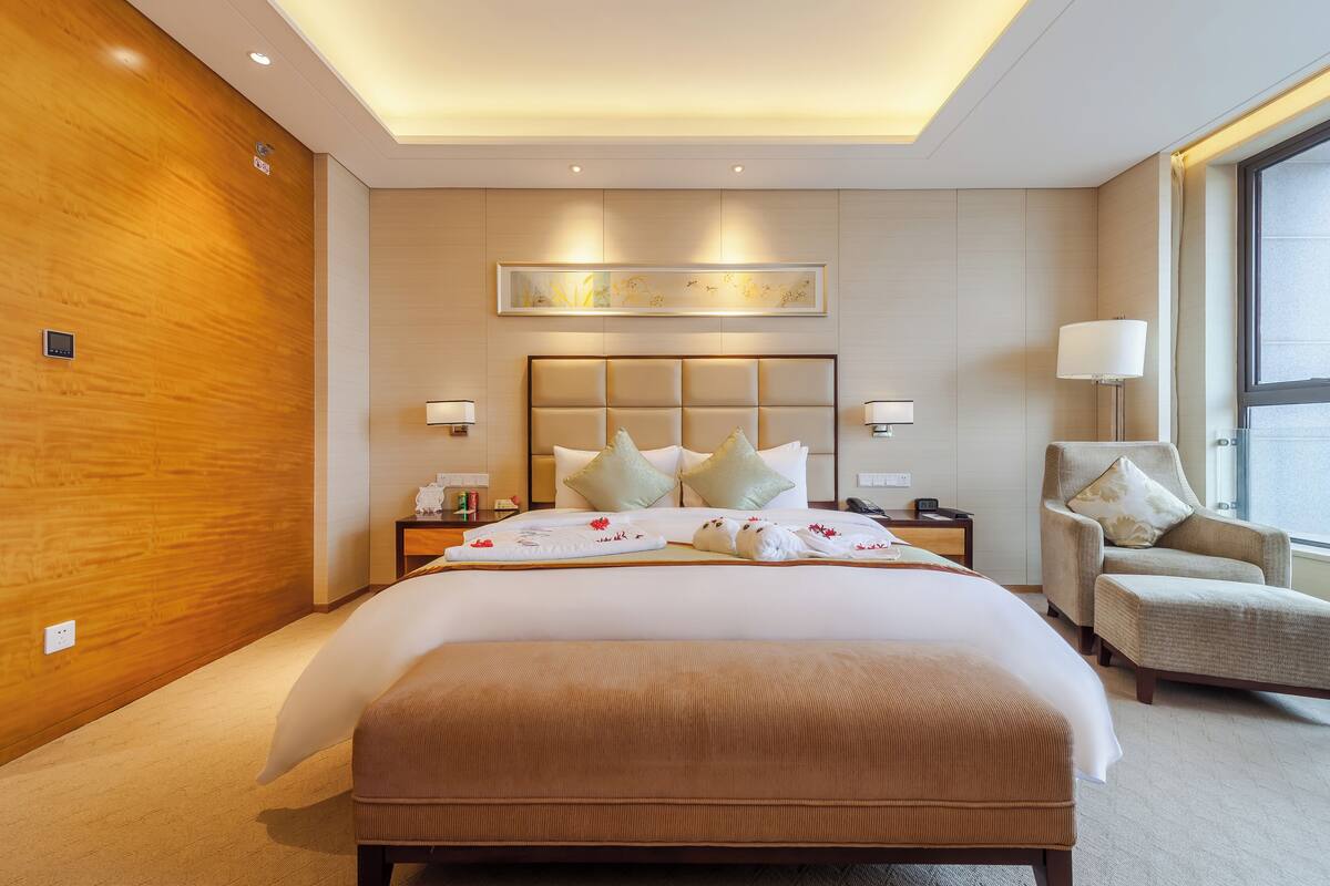 Ein Hotelzimmer mit einem großen Bett, einem Sessel, einem Nachttisch und einem Fenster.