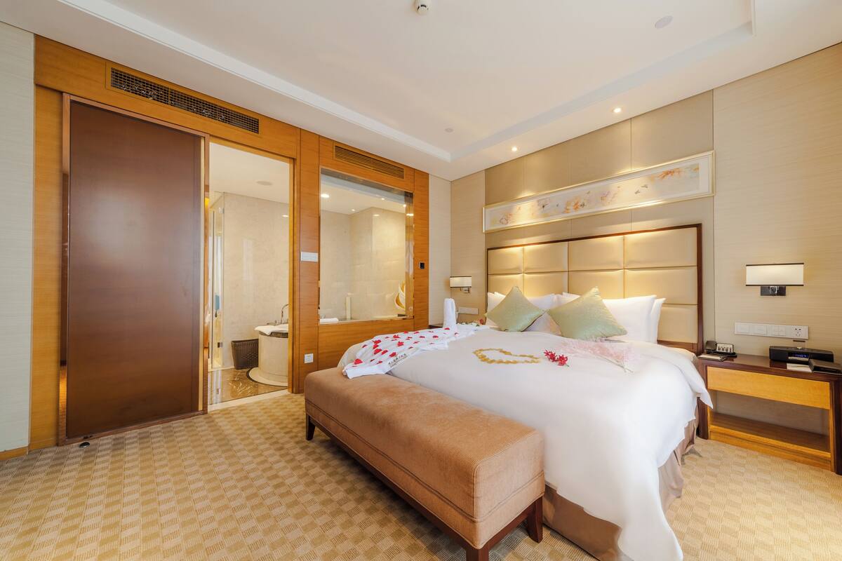 Ein Hotelzimmer mit einem großen Bett, einer Bank, einem Nachttisch und einem Spiegel.
