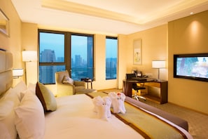 A hotel room with a large bed, two chairs, a desk, a television, and a city view.