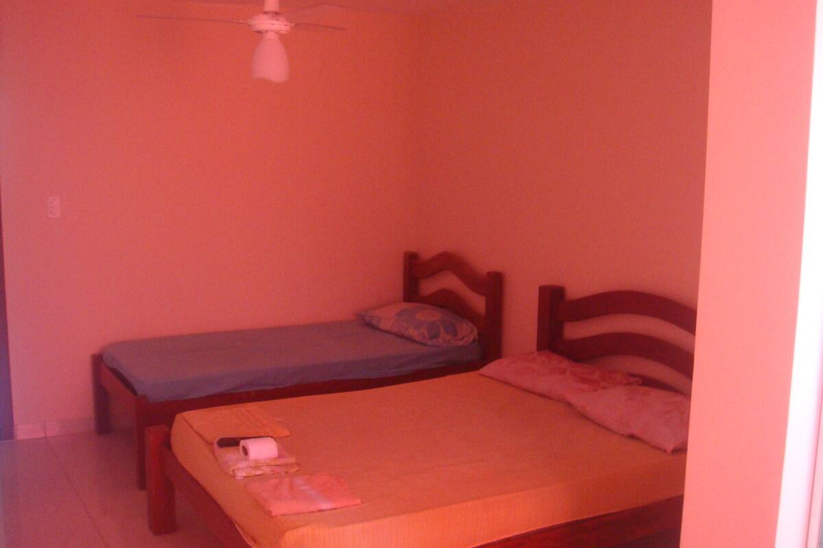 Ein kleines Zimmer mit zwei Einzelbetten, einem Deckenventilator und einer schlichten Wand.
