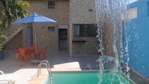 A swimming pool with a waterfall feature, outdoor seating, and a brick building in the background. - Stellamares Apartamentos (Salvador)