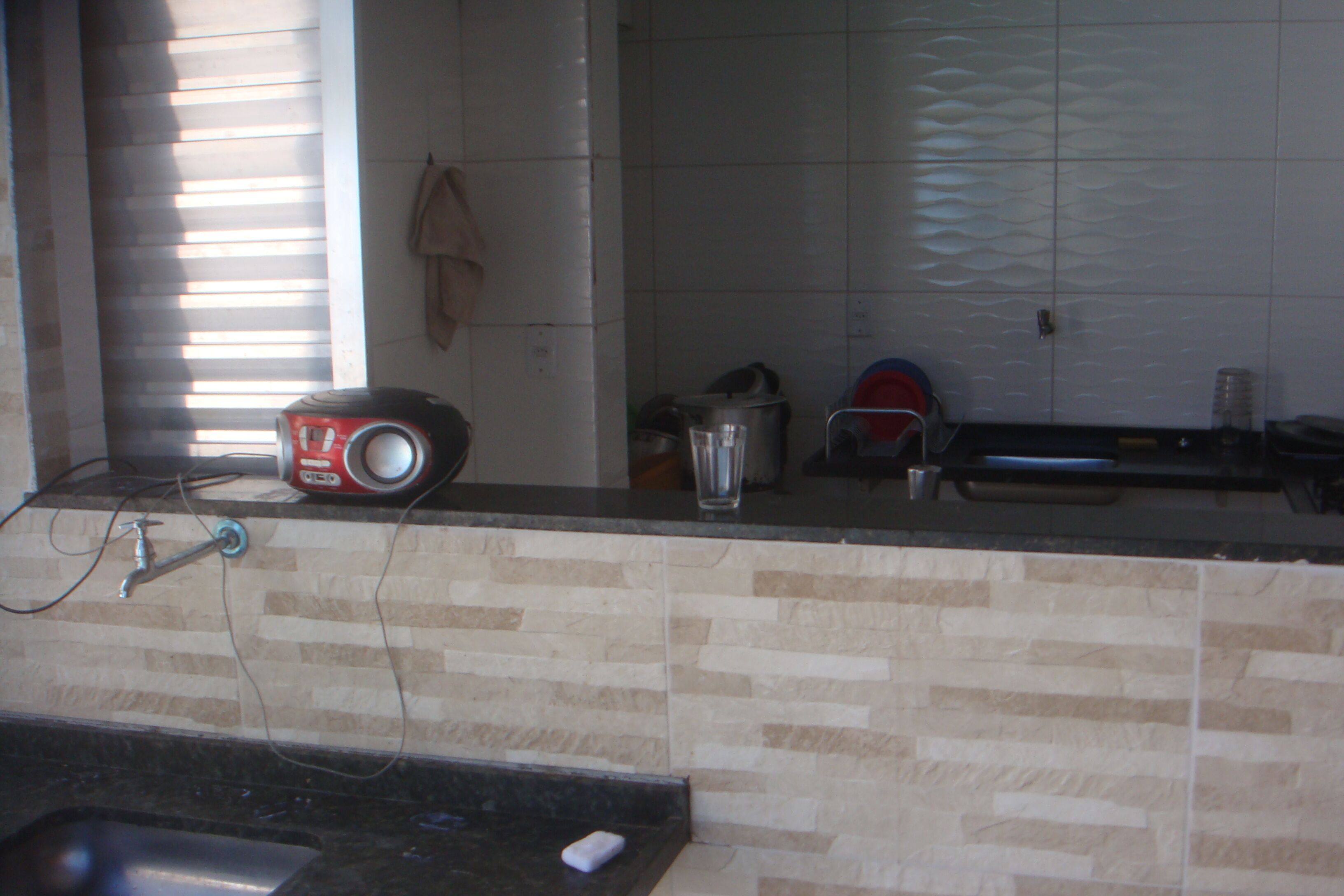 A kitchen with a tiled backsplash, a sink, a countertop with a kettle, a pot, and a glass.