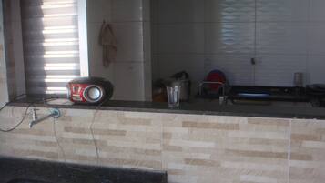 A kitchen with a tiled backsplash, a sink, a countertop with a kettle, a pot, and a glass.