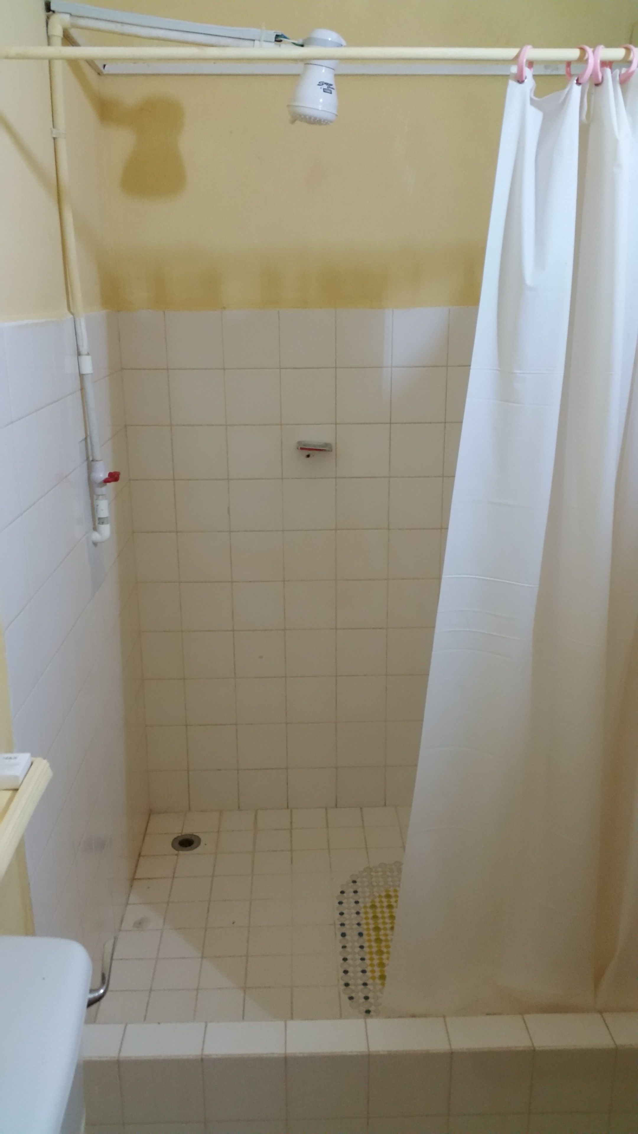 A shower area with a white curtain, tiled walls, and a drain at the bottom.
