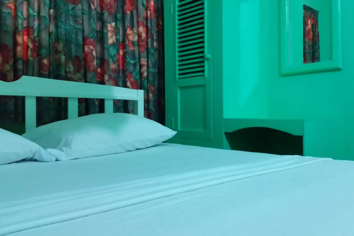 Ein Bett mit weißer Bettwäsche, einem blumigen Vorhang und einer grünen Wand.