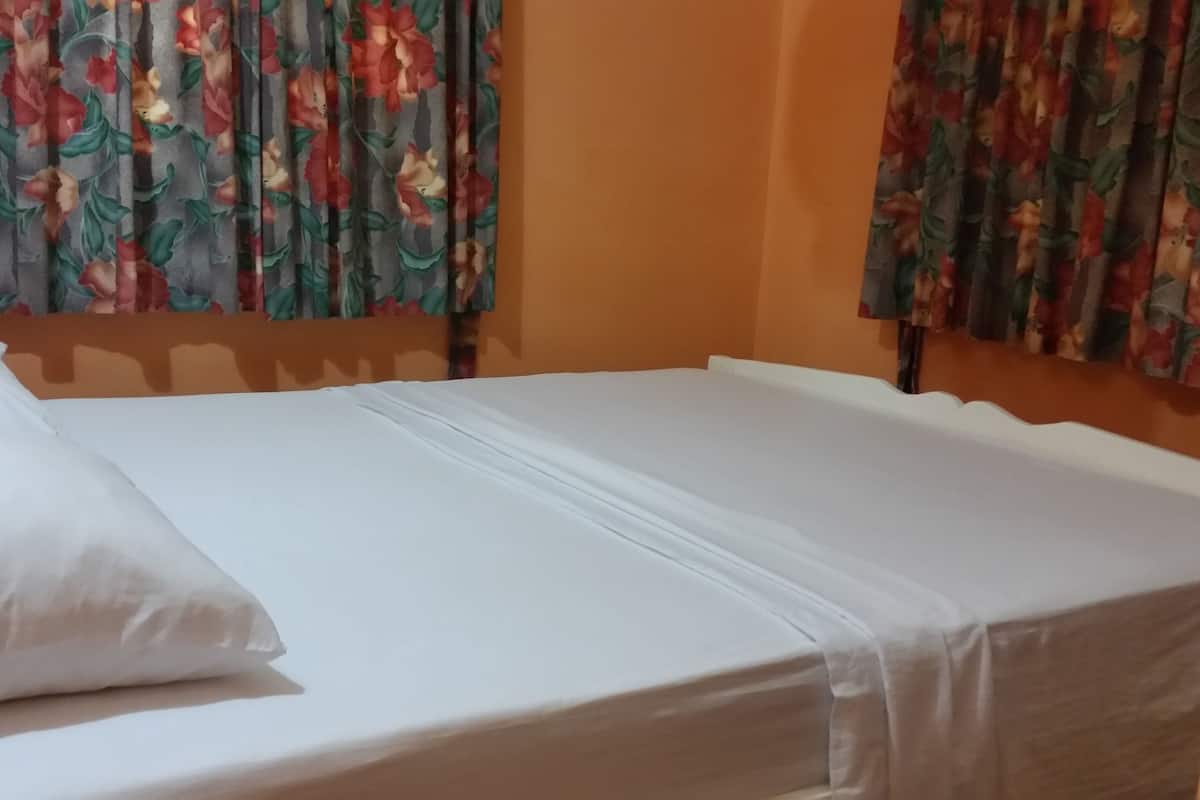 Ein Bett mit weißen Laken und Kissen, ein Holz-Kopfteil und blumige Vorhänge.