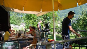 Ein Essbereich im Freien mit Tischen, Stühlen, einem Grill und Blick auf ein bewaldetes Gebiet.