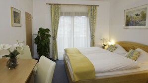 Ein Hotelzimmer mit einem hölzernen Bett, einem Schreibtisch, einem Stuhl, einer Zimmerpflanze und zwei Bildern an den Wänden.