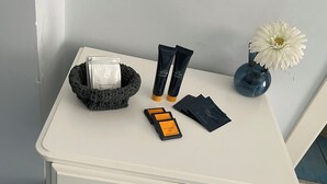 A white bedside table with toiletries, a vase with a white flower, and a black basket. - CAPRI B&B (Salerno)