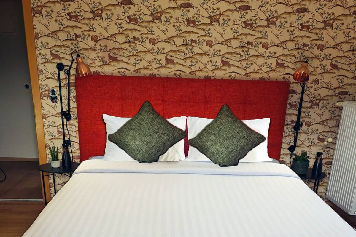 A bed with a red headboard, white bedding, and two green pillows.
