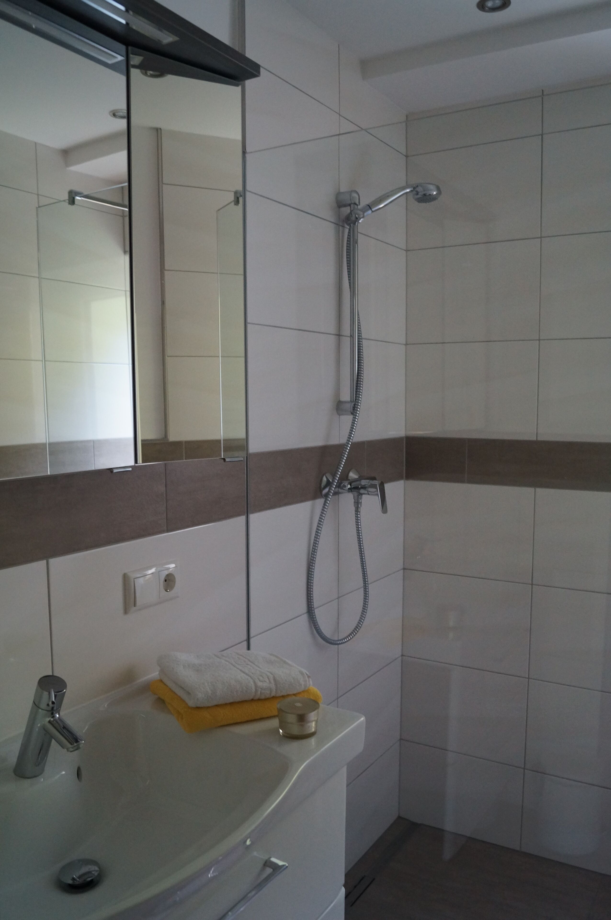 Un baño con lavamanos, espejo, ducha y perchero para toallas.