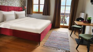 Un dormitorio con una cama roja, un escritorio de madera y vistas a montañas a través de la ventana.