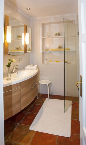 Ein modernes Badezimmer mit einem gebogenen Waschtisch, einer Duschkabine aus Glas und einem kleinen Hocker.