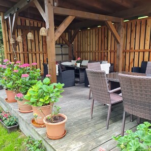 Eine Terrass mit Gartenmöbeln aus Holz, Kübelpflanzen und einem Grillbereich.