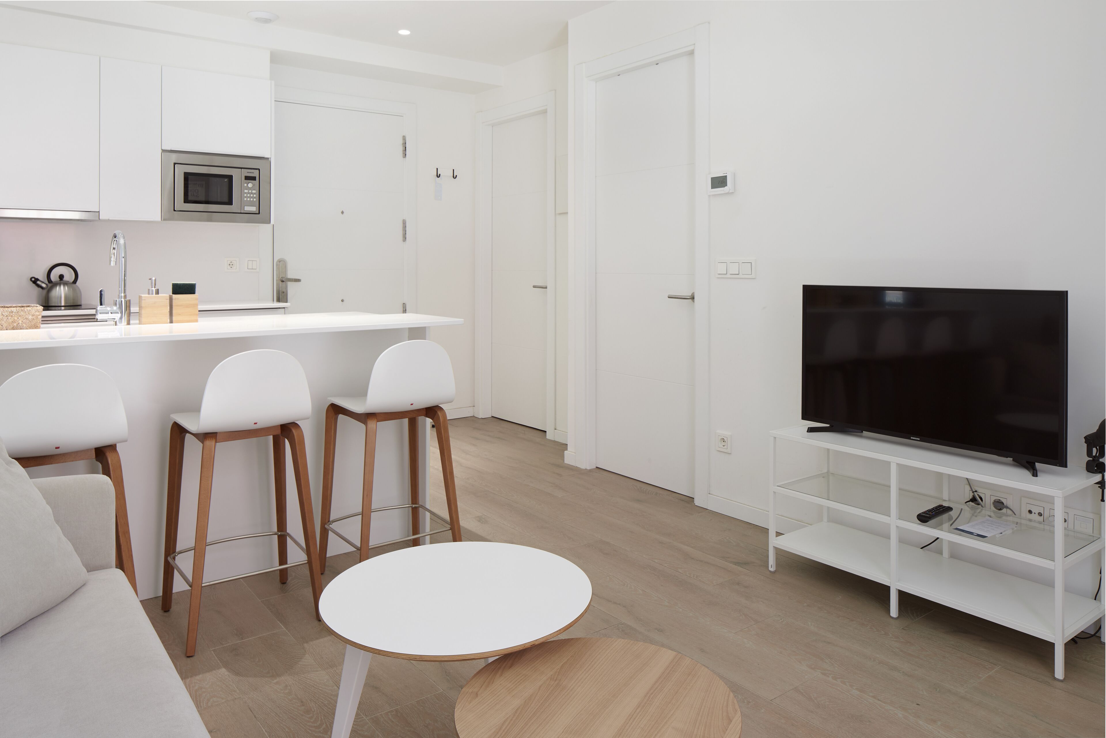 A modern kitchen with white cabinets, a microwave, and a bar area with stools.