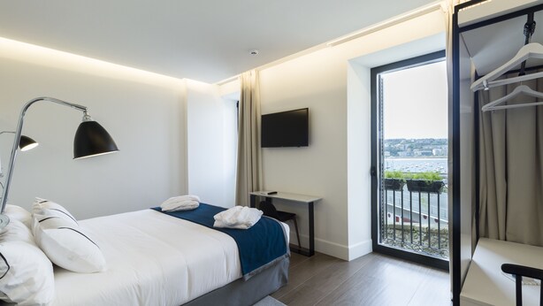 Habitación de hotel moderna con una cama grande, un escritorio, un televisor y un balcón con vistas a la ciudad.