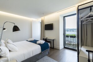 A modern hotel room with a large bed, a desk, a TV, and a balcony with a city view. - Hotel SANSEbay (San Sebastián)