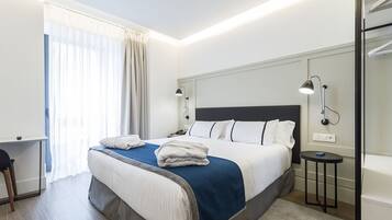 Una habitación de hotel moderna con una cama grande, lámparas de noche, un escritorio y vistas al exterior.