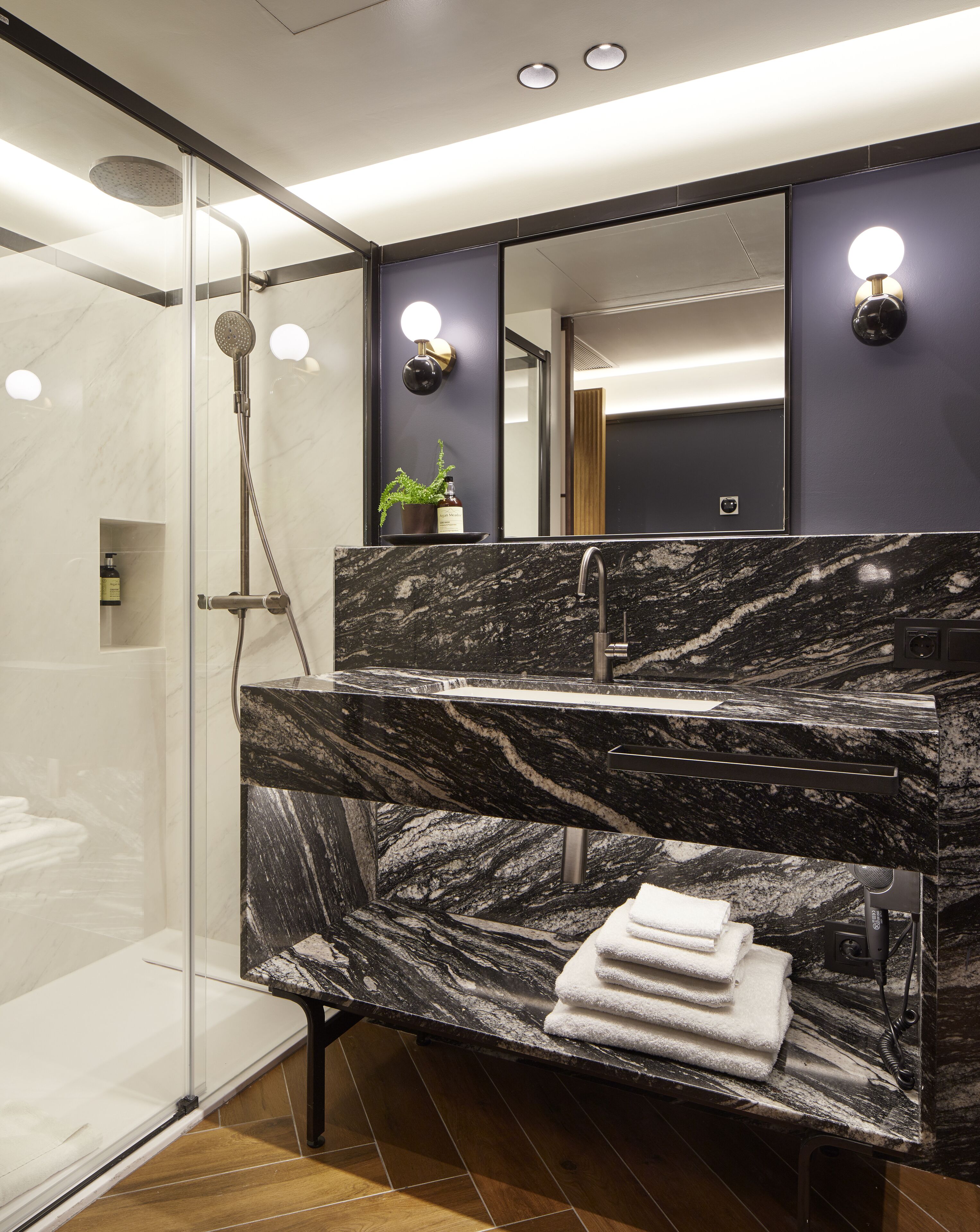 A modern bathroom with a glass-enclosed shower, a marble sink, and a large mirror.