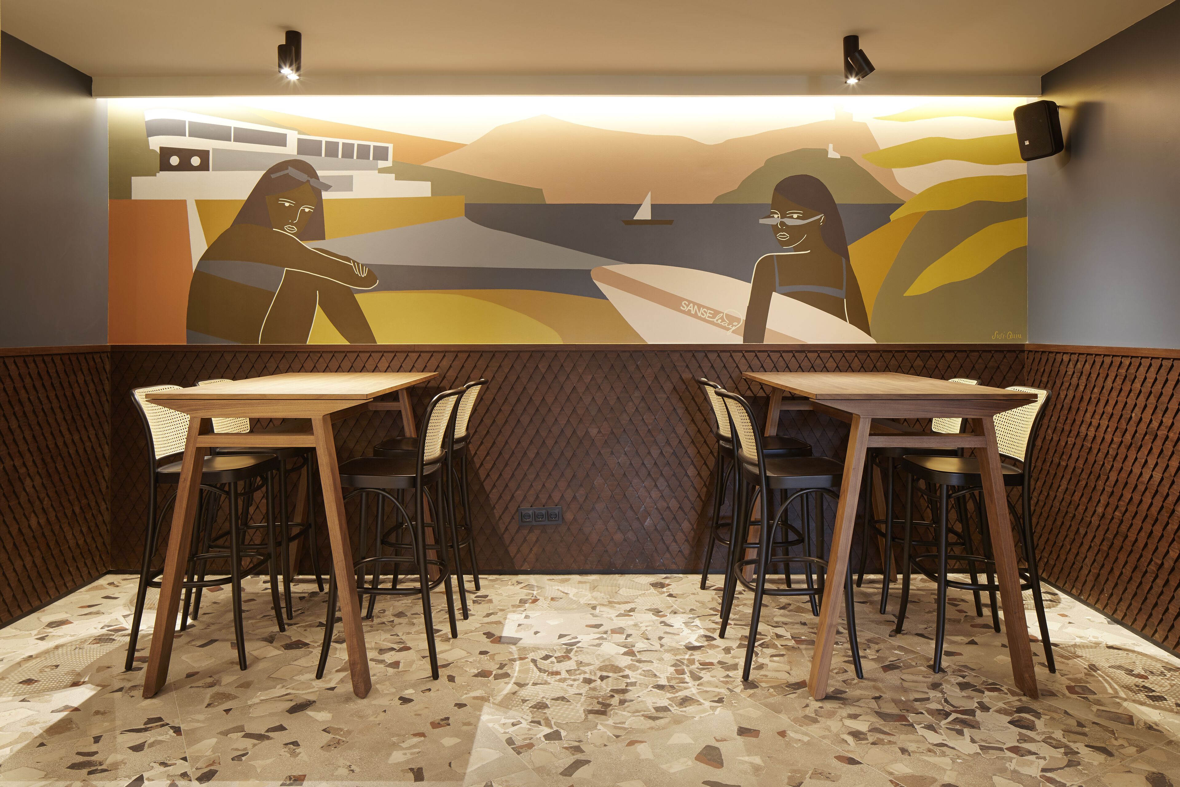 Ein Restaurant mit Wandmalerei einer Küstenszene, Holztischen und -stühlen sowie einem gemusterten Boden.