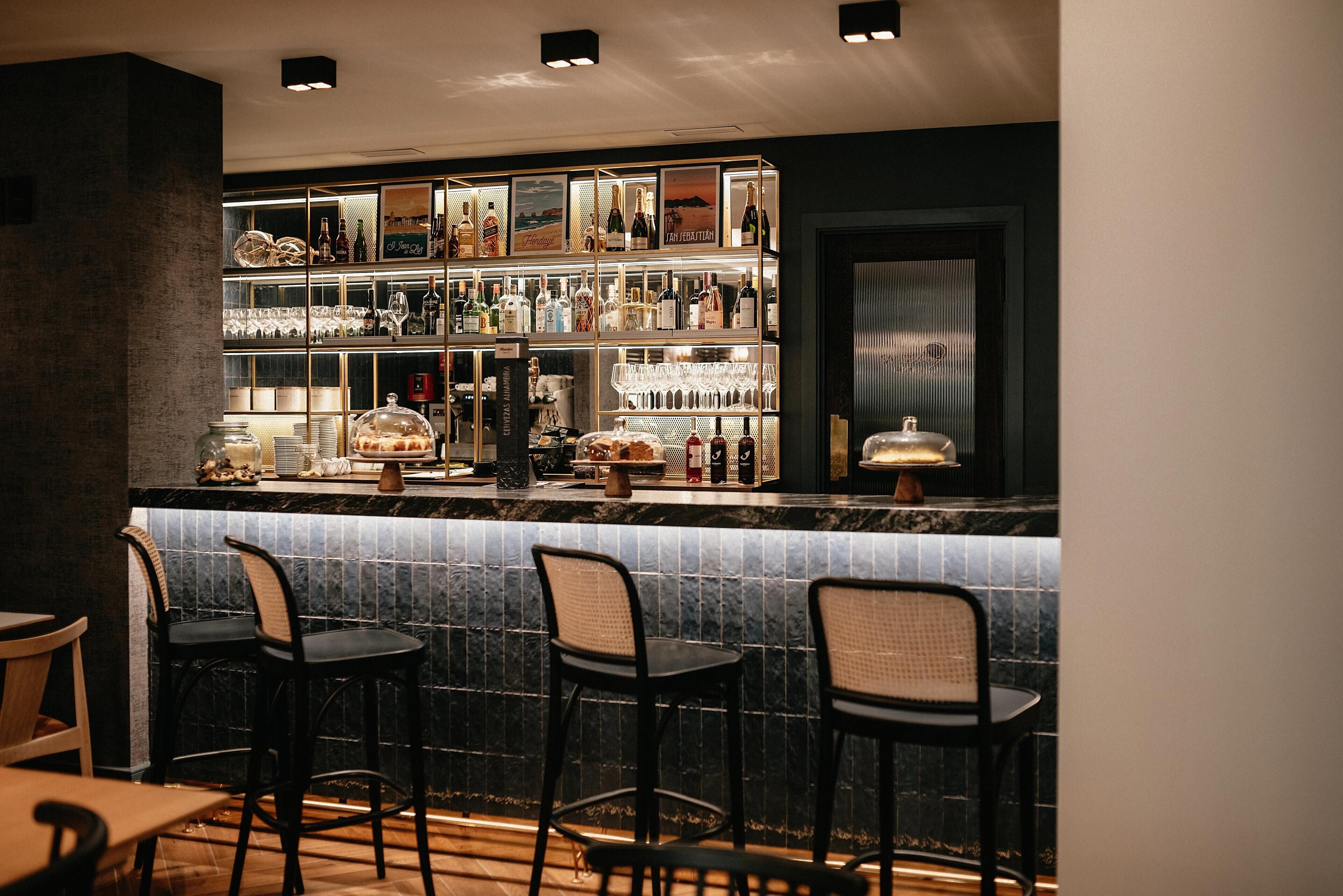 A bar area with a marble countertop, bar stools, and shelves stocked with bottles and glasses.