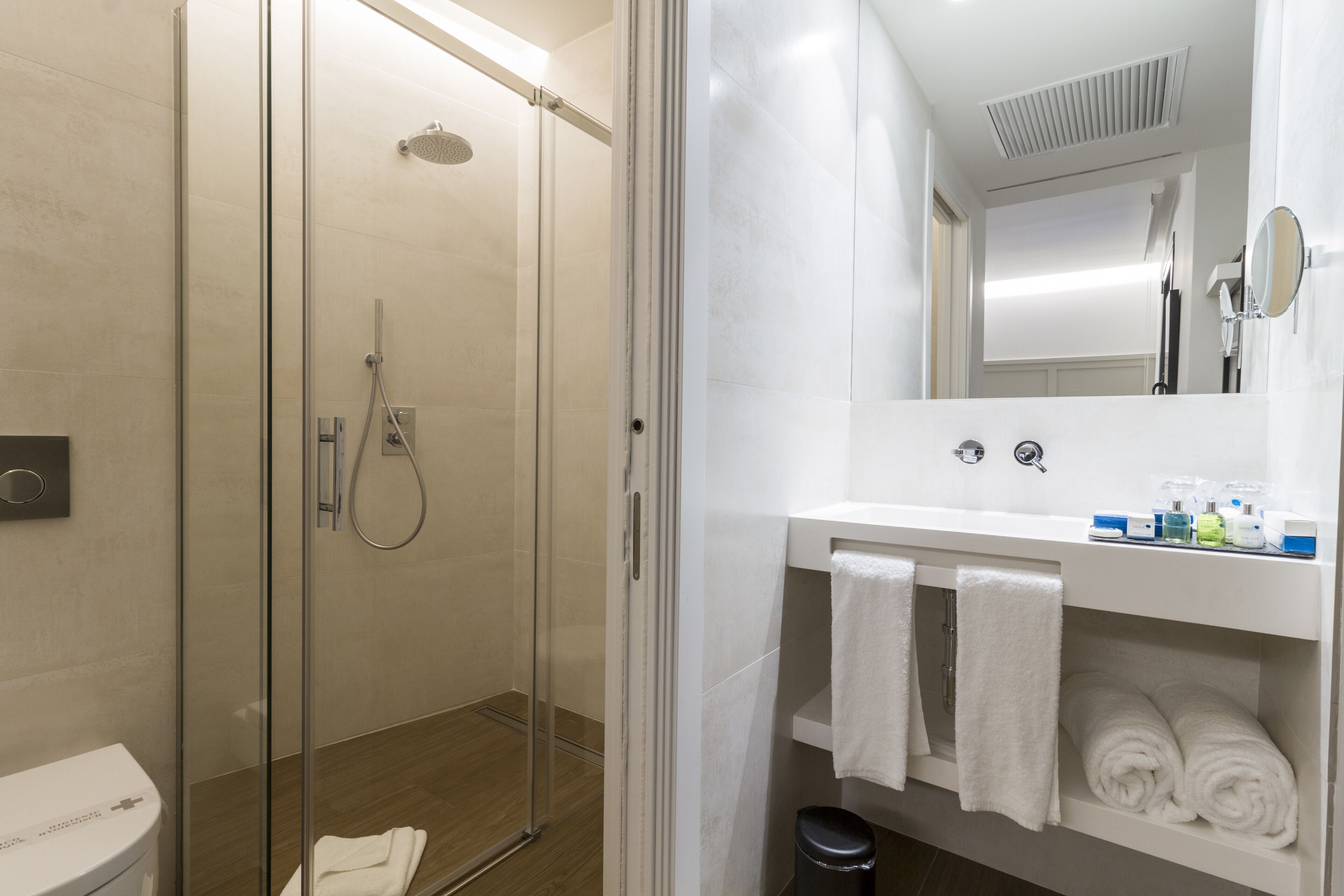 A modern bathroom with a glass-enclosed shower, a white sink with a mirror, and neatly folded towels.