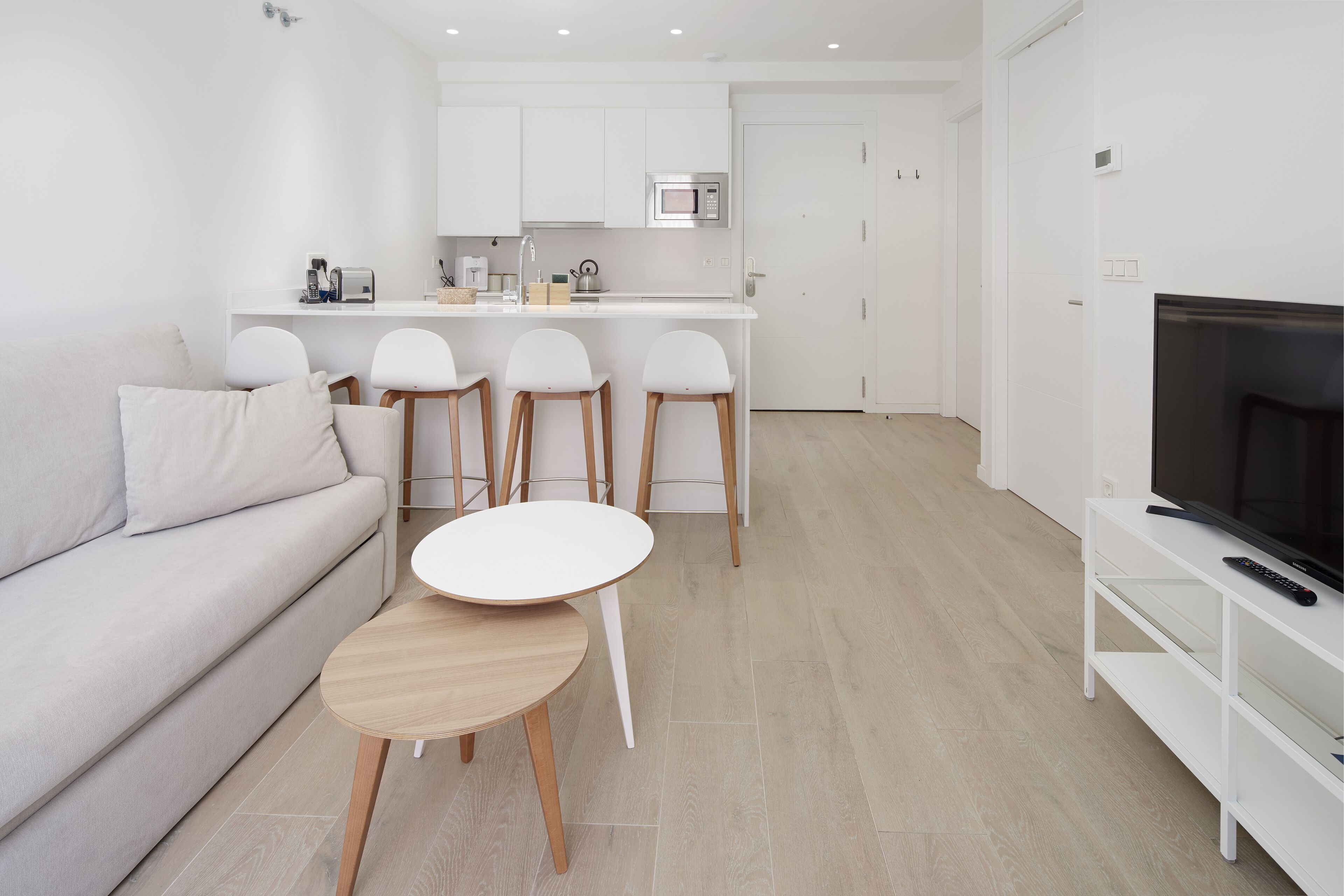 A modern living room with a sofa, a small round table, and three bar stools.