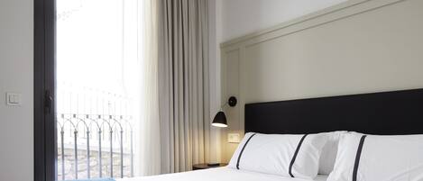 A hotel room with a bed, a nightstand, a lamp, and a view of the outside.