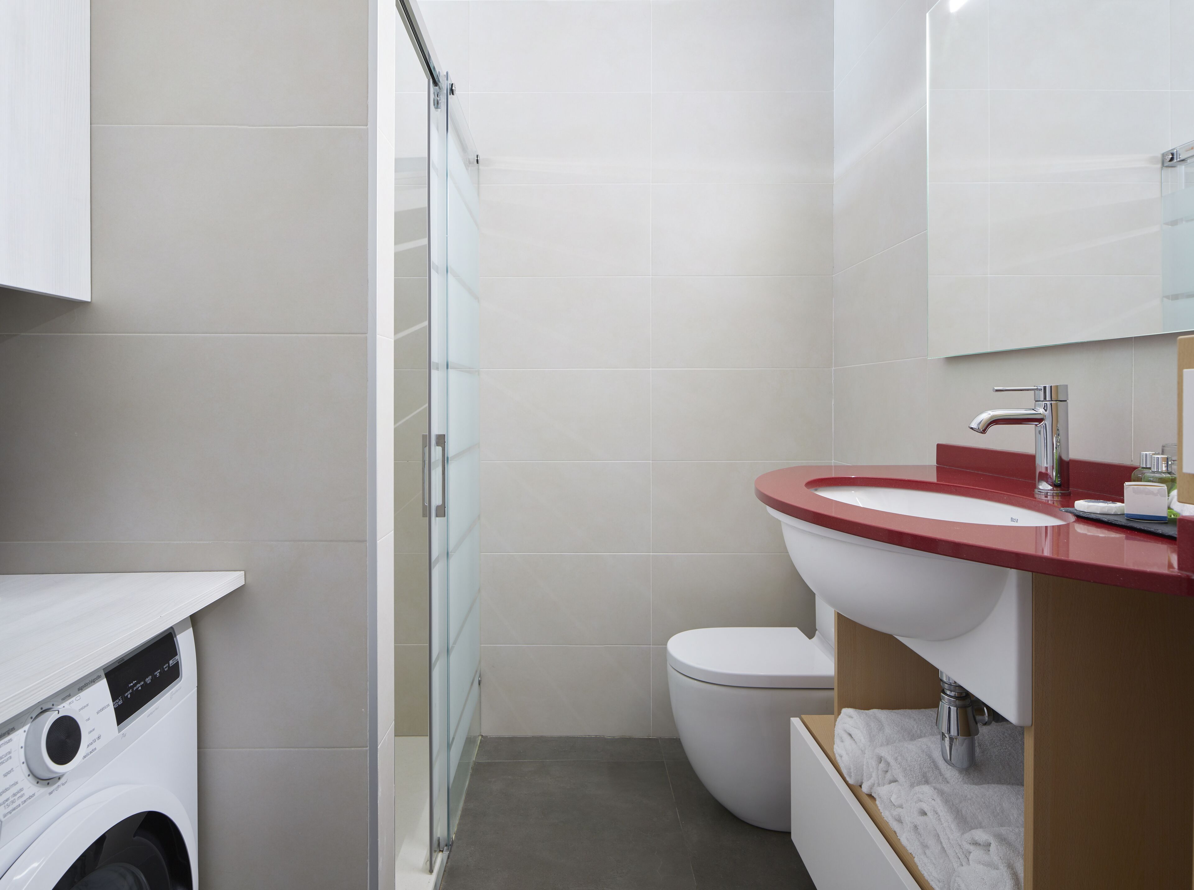 Une petite salle de bain dotée d’une douche à parois de verre, de toilettes blanches et d’un lavabo rouge avec un miroir au-dessus.