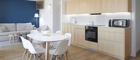 A modern kitchen with wooden cabinets, a microwave, and a stove. There is a dining area with a white table and chairs.