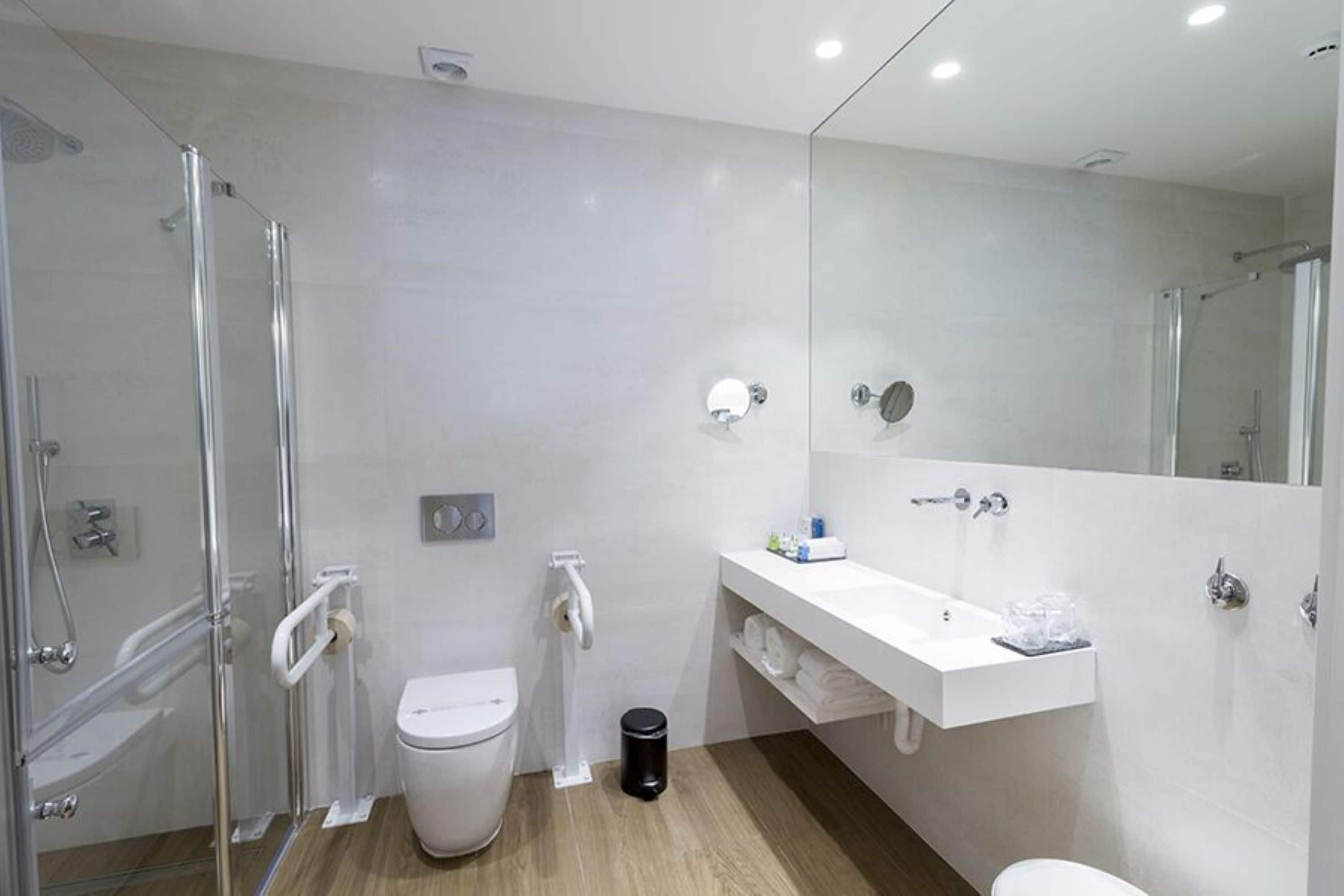 A modern bathroom with a glass shower enclosure, a white toilet, a vanity with a mirror, and a sink.