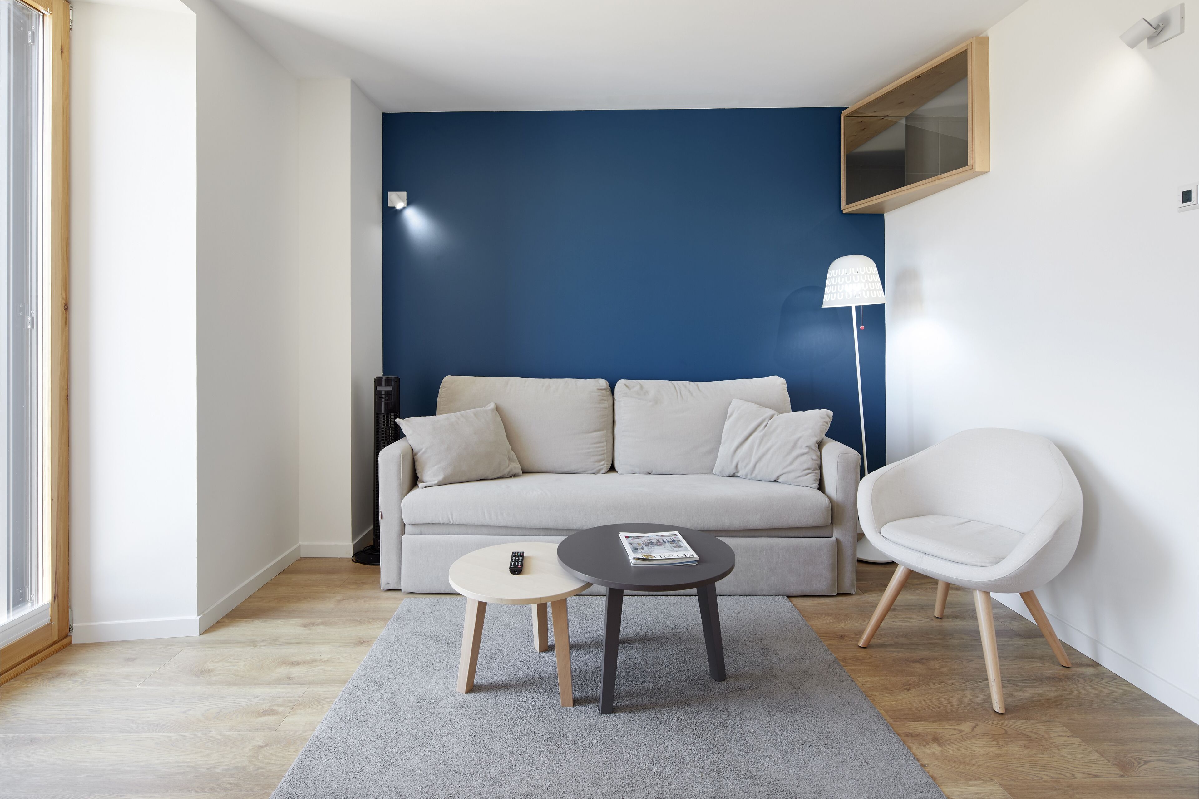 A modern living room with a sofa, two tables, a lamp, and a window.