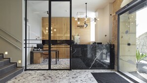 Un área de recepción de hotel con diseño moderno, que incluye un mostrador de mármol, un mostrador de madera y una escalera que conduce a los pisos superiores.