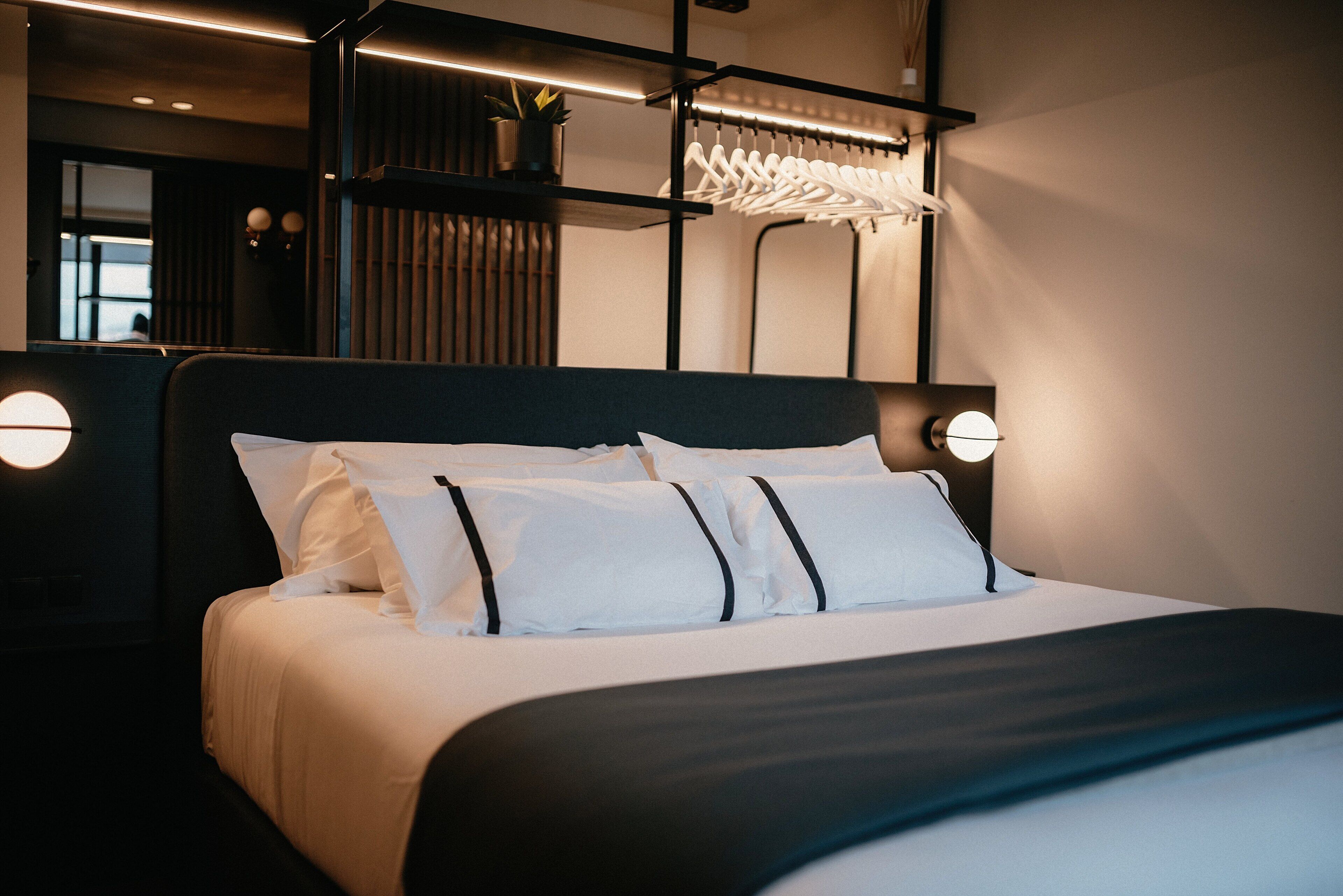 A neatly made bed with white linens and black accents, a black headboard, and two wall-mounted lamps.