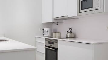 A modern kitchen with white cabinetry, a built-in oven, a microwave, and a kettle on the countertop.