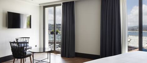 Een hotelkamer met een bed, een aan de muur bevestigde televisie, een balkon met gordijnen en uitzicht op zee.