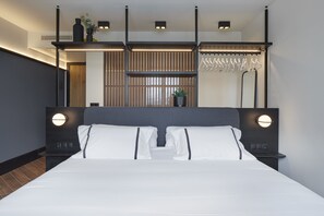 A modern hotel room with a large bed, two bedside tables, a wall-mounted shelf with decorative items, and a hanging coat rack. - Hotel SANSEbay (San Sebastián)