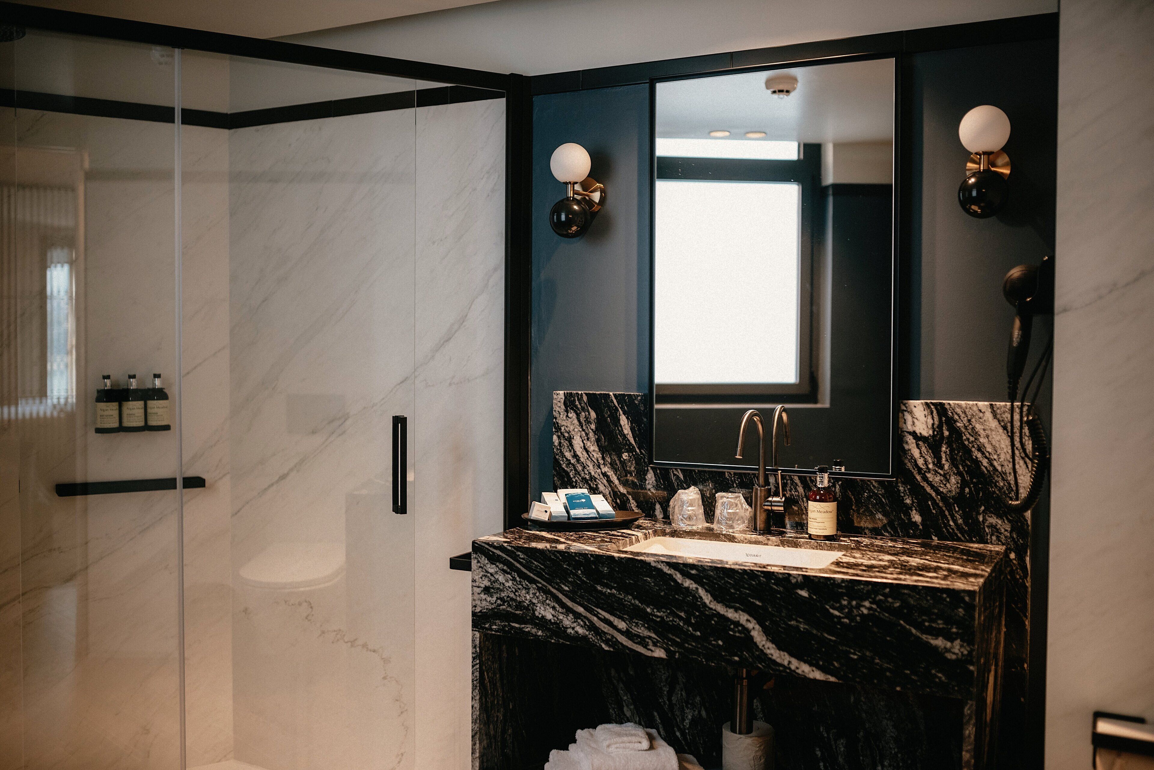 Une salle de bain moderne avec un lavabo en marbre, un grand miroir et une douche à parois de verre.