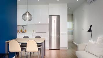 A modern kitchen with white cabinets, a stainless steel refrigerator, and a dining area with a wooden table and chairs.