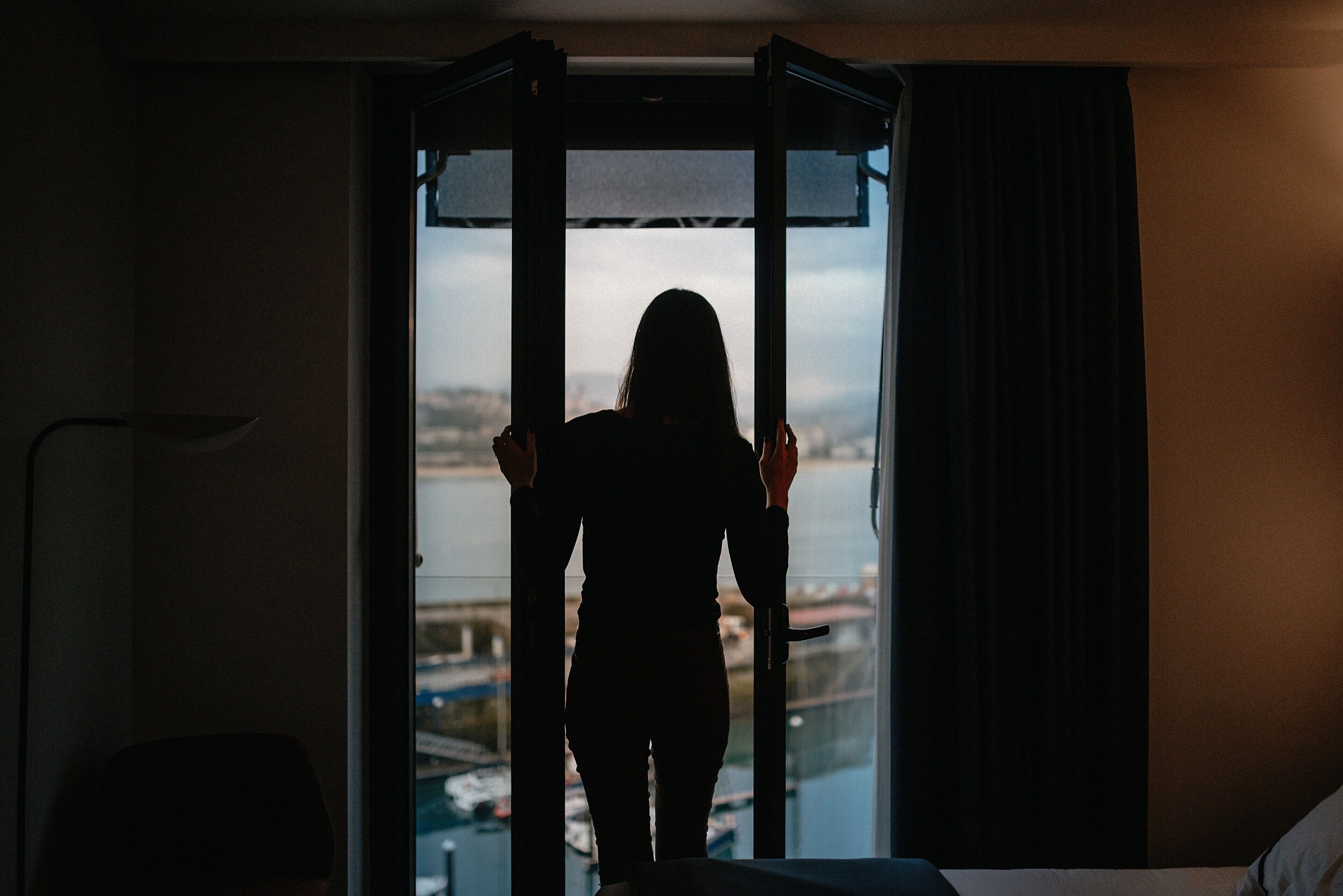 A person standing at a window with a view of a body of water and buildings.