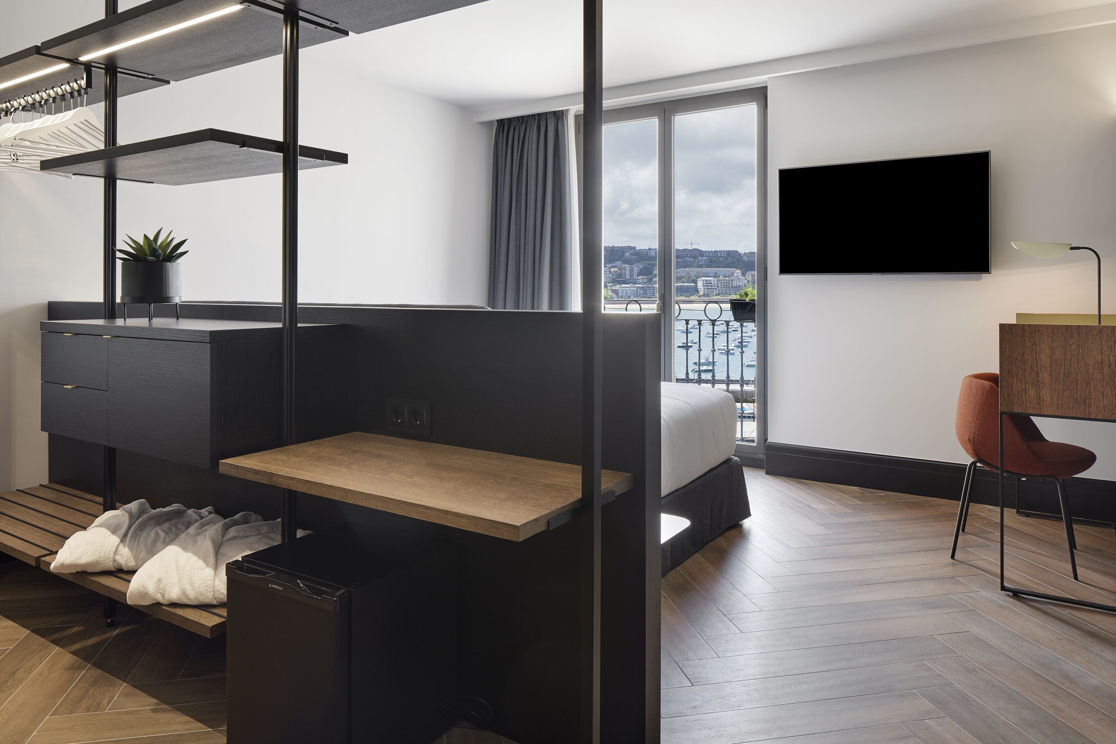 Una habitación de hotel moderna con cama, escritorio, silla, televisor y balcón con vista a la ciudad.