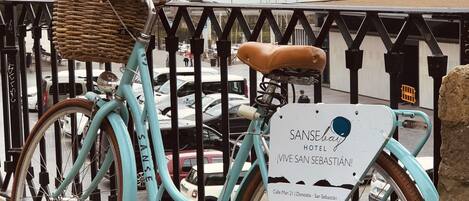 A turquoise bicycle with a wicker basket and brown leather seat parked on a stone-paved area.