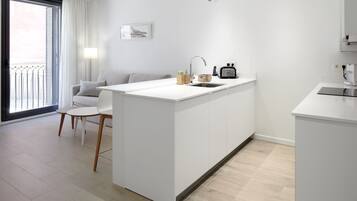 Cocina moderna con una isla central, un comedor con mesa y sillas blancas, y vistas al exterior a través de un ventanal.