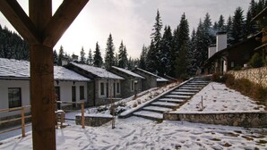 A snow-covered outdoor area with stone steps leading to a building with multiple windows. - Holiday Village Kochorite (Smolyan)