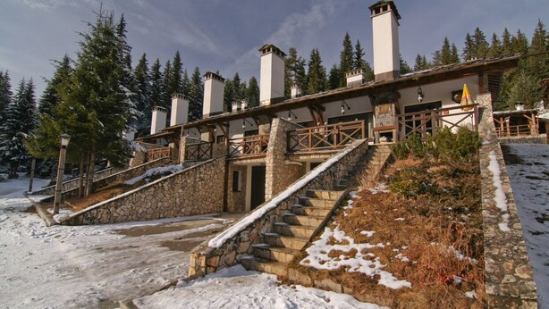 A stone building with a wooden staircase leading to a door, surrounded by snow and trees. - Holiday Village Kochorite (Smolyan)