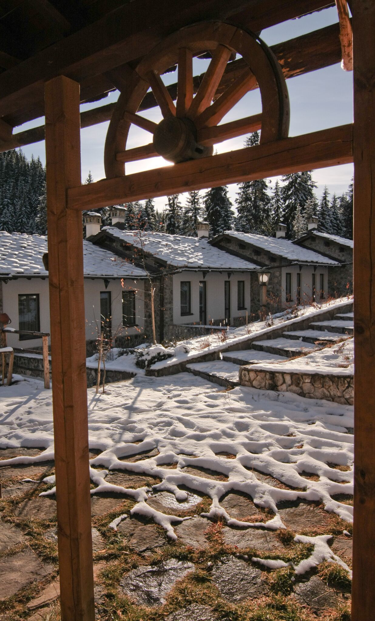 A wooden pergola structure with a snow-covered landscape and buildings in the background.