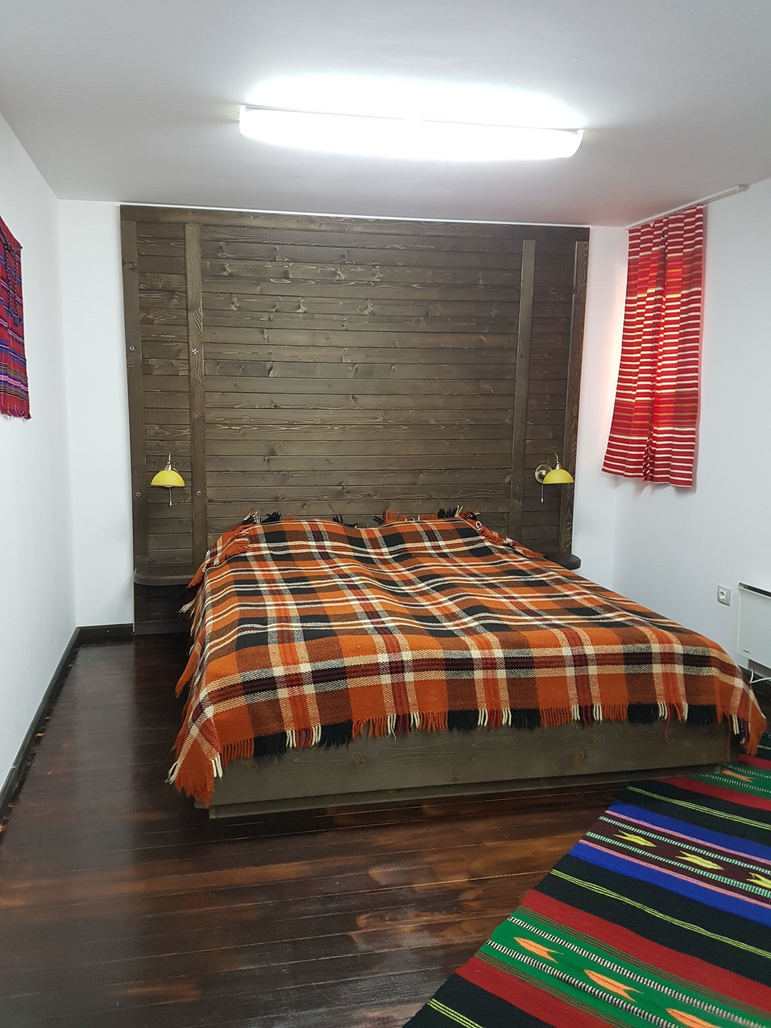 Une chambre avec une tête de lit en bois, une couvre-lit à carreaux et un tapis coloré.