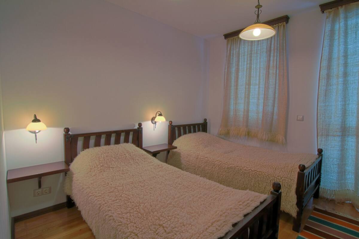A bedroom with two beds, a nightstand, a lamp, and a window with curtains.