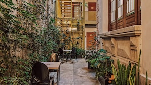 Un couloir intérieur étroit, avec un escalier, des plantes en pot et des tables avec des chaises.